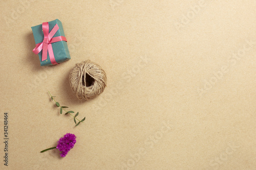 Gift box and string with dry flowers on kraft paper background. Flat lay, top view, copy space