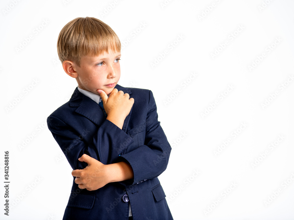 Confident blond boy dressed in a formal suit with blue tie. Serious kid in a blue business suit, posing at studio. Photo of a cute little businessman boy. Leader conception. Confident blond boy dressed in a formal suit with blue tie. Serious kid in a blue business suit, posing at studio. Photo of a cute little businessman boy. Leader conception.