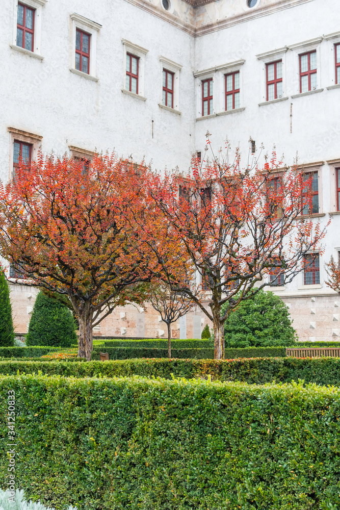 Courtyard of a historic castle complex in Trento, Italy. Redleaved autumn Trees mark the way.