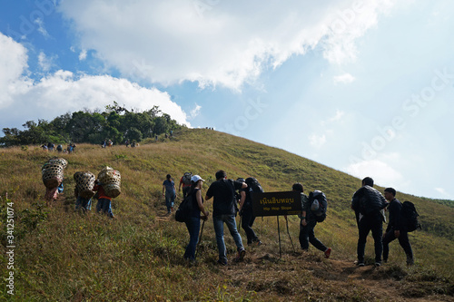 A group of tourists trekking along grassy trail pathway to green mountain peak