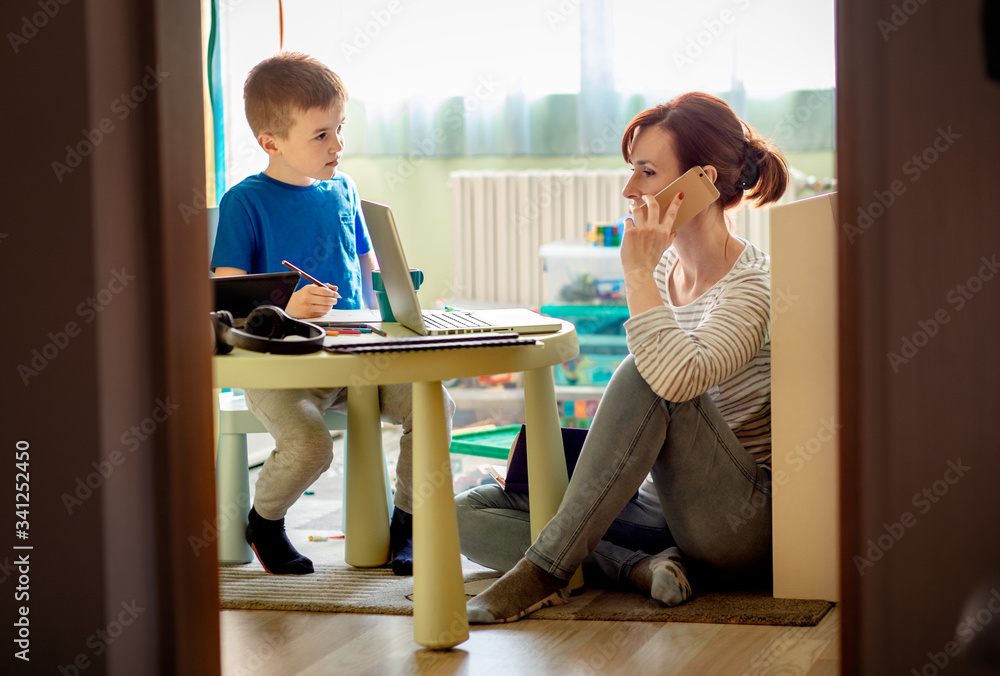 Mother working remotely on laptop while taking care of her son playing with toys in his room. Mother working remotely on laptop while taking care of her son playing with toys in his room.