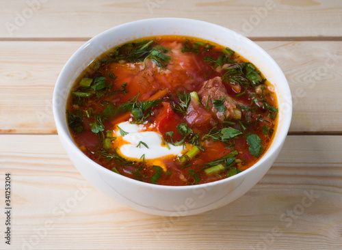 Borsch with sour cream in a white bowl on a wooden background. Side view