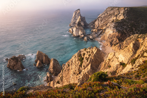 Sunset at Praia da Ursa Beach. Rocky cliff ridge with sea stack in atlantic ocean lit by evening warm light. Holiday vacation in Sintra region, Portugal