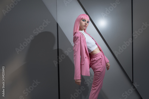 Bilde på lerret Young woman in pink pant suit with pink hair on metallic, business centre wall background