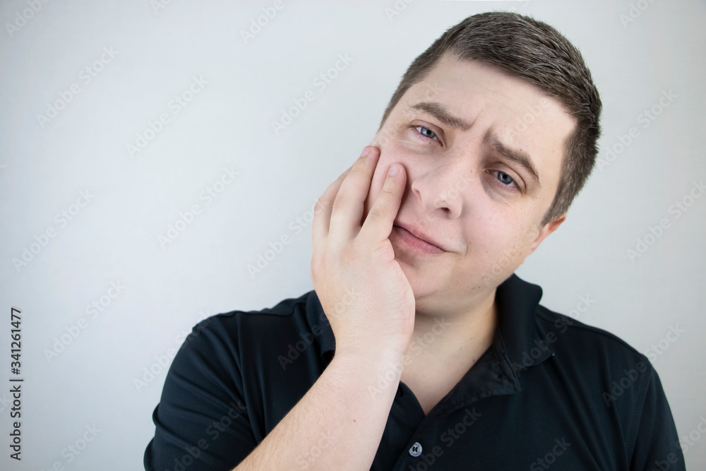 A man clings to his cheek and winces in pain in his tooth. The concept of dental problems, caries, tooth decay, flux. White background and place for text. A man clings to his cheek and winces in pain in his tooth. The concept of dental problems, caries, tooth decay, flux. White background and place for text.