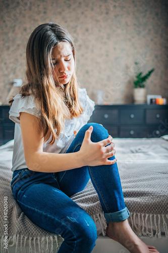 girl sitting on bed clutching a sore knee