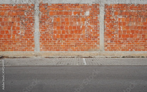 Wall made with different types of bricks and strips of cement. Sidewalk and asphalt road in front. Urban  background for copy text
