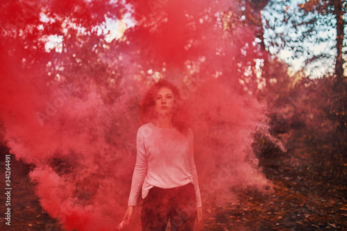 Beautiful red-haired woman with pink smoke bomb screen in the woods.