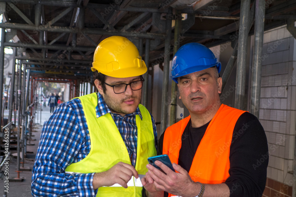 Construction workers at work on construction site using an electronic device. Outdoors Construction workers at work on construction site using an electronic device. Outdoors