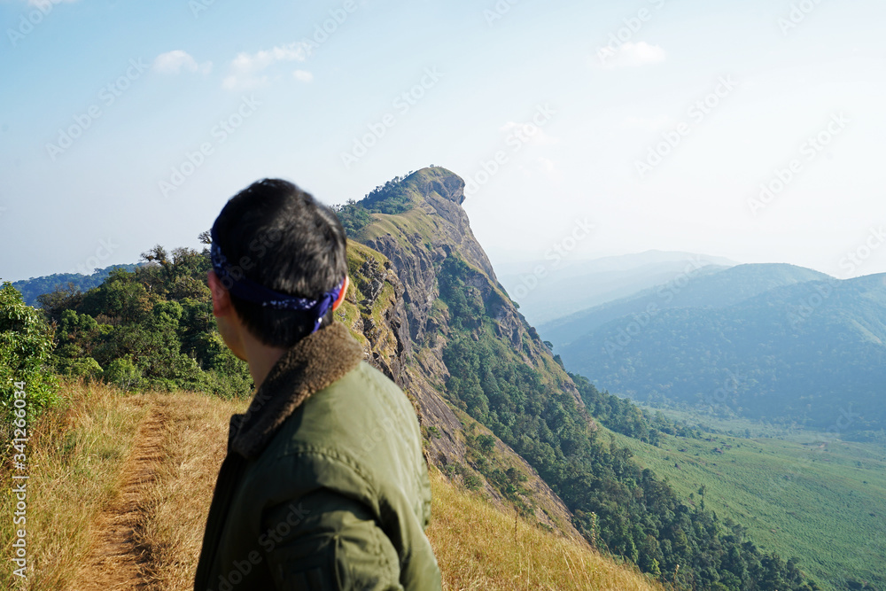 A man standing on the peak looking at green mountain range with cloudy sky