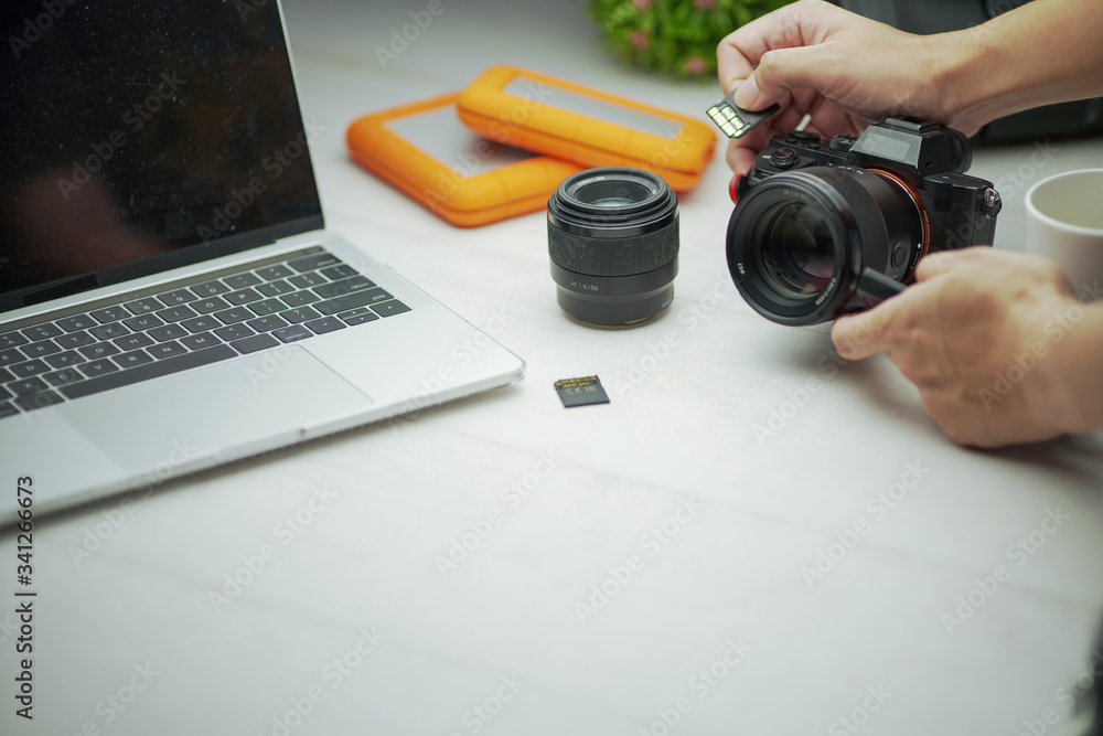 hands insert the memory card to the professional camera in modern design coworking space, work desk with laptop and professional camera