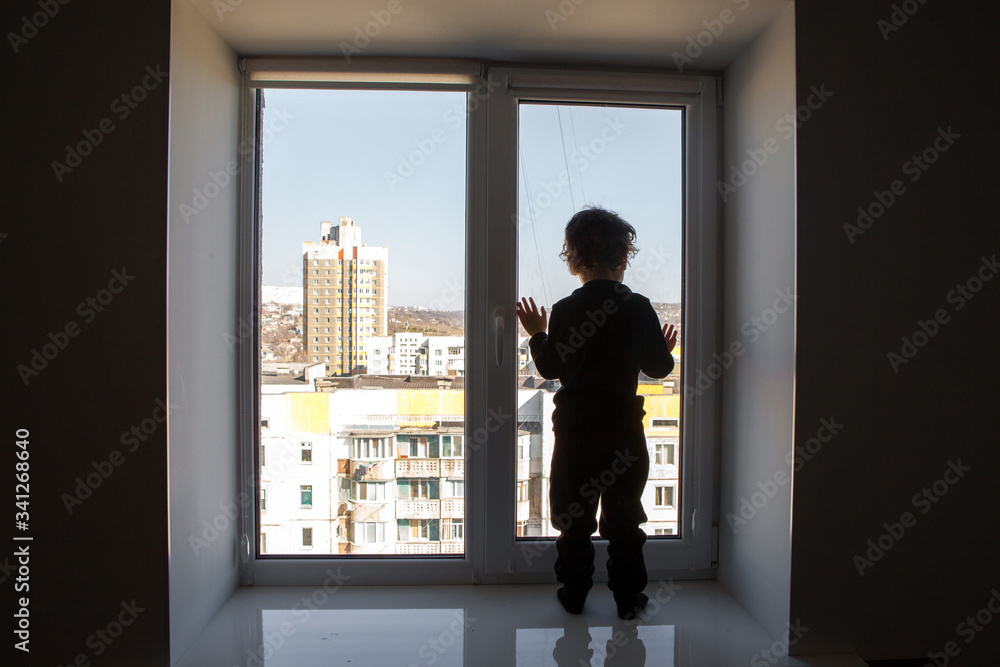 Fototapeta premium stay at home. A child stands on a windowsill and looks at an empty deserted street during the worldwide quarantine of the coronavirus pandemic.