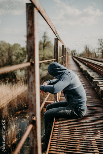 A man dangled his legs from the edge of the bridge and looks down