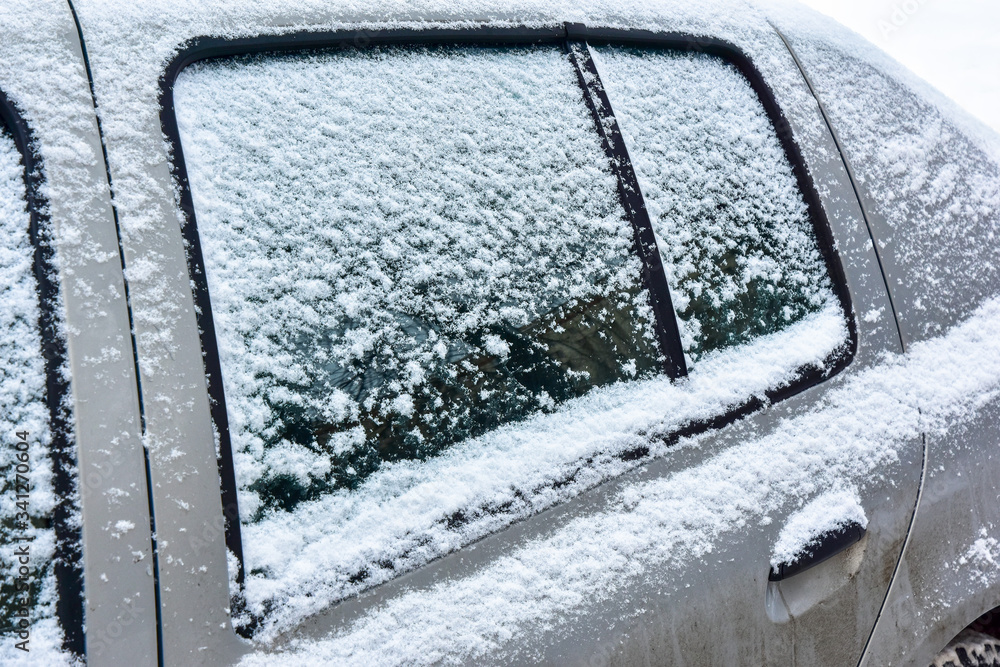 Fragment of a grey car covered with white snow close-up