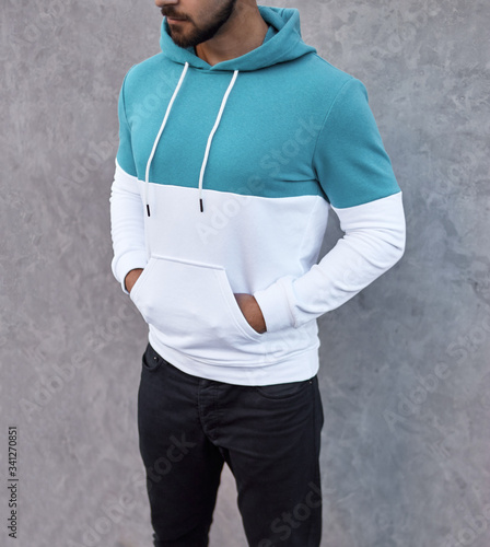 young man in white and torqouise hoodie standing outdoors on gray background photo