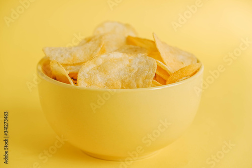 Potato chips in a yellow bowl on a yellow background. Copy, empty space for text