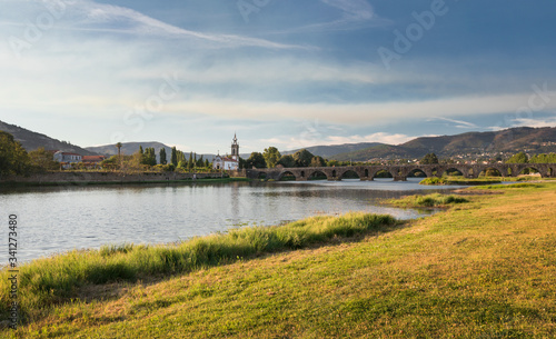 Bridge Ponte de Lima with church during afternoon on sunny day, river Lima and green grass on riverside, Portugal.