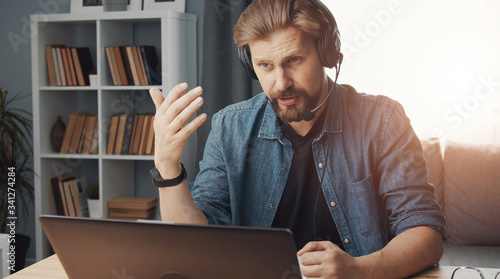 Casual-dressed man teleworking sitting in front of computer with headset on, selfisolation, epidemic photo
