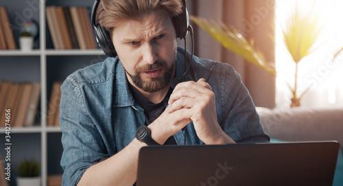 Front view of dutiful man with headset doing distance work looking at computer screen, lockdown photo
