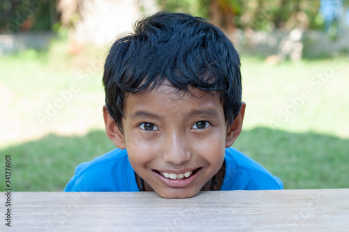 The boy sit smile and placed his chin on a wooden table in the lawn.