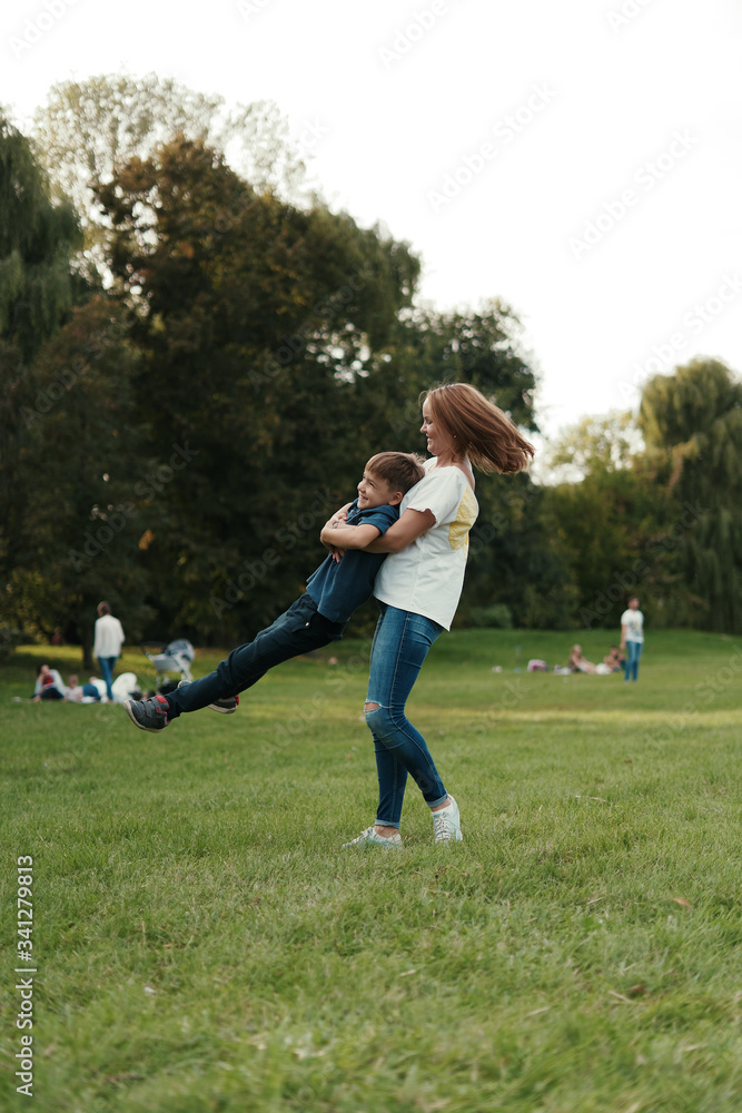 Lovely young mother playing with her preschool on the grass in the park, they are making roundabouts Lovely young mother playing with her preschool on the grass in the park, they are making roundabouts