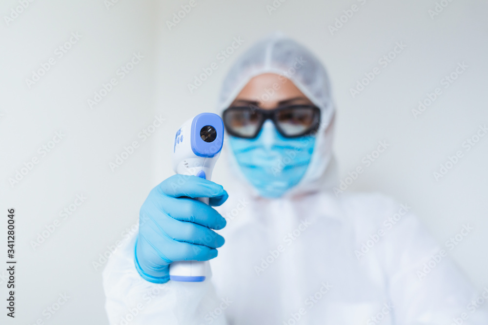 Naklejka premium Doctor holding infrared thermometer. Portrait of medical professional in protective clothing measuring contactless fever at Covid-19 test center during coronavirus epidemic.