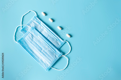 Disposable protective face masks and white pills and copy space on blue background. COVID epidemic. Flu and virus hygiene, top view