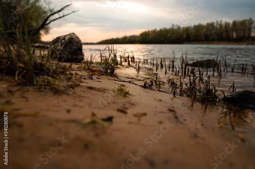 Sunset on the lake. Glare on the surface of the water. The bright rays of the sun. Landscape of a river with stones on the shore