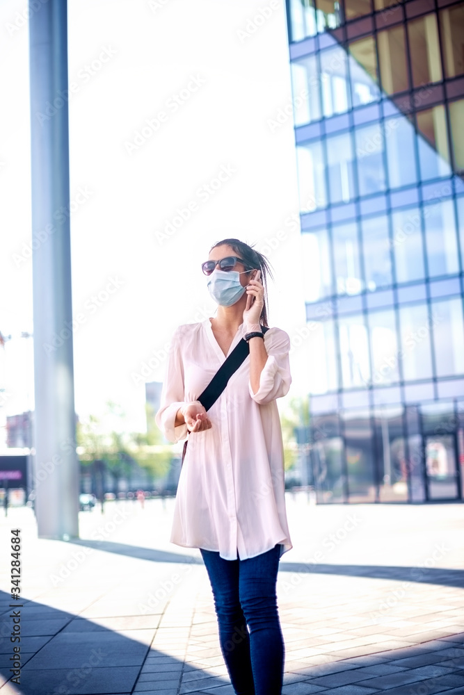 Fototapeta premium Casual businesswoman wearing face mask and making call during coronavirus pandemic in the city