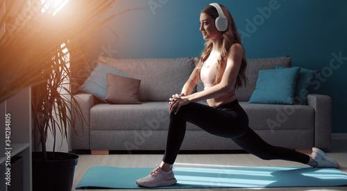 Fotografie Fitness girl in athletic clothes and headphones doing forward lunge training leg