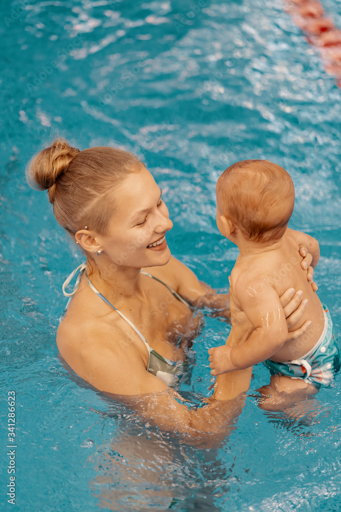Young mother and her baby enjoying a baby swimming lesson in the pool. Child having fun in water with mom Young mother and her baby enjoying a baby swimming lesson in the pool. Child having fun in water with mom