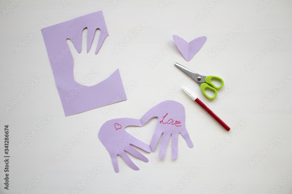 © Diana - Child made a greeting card. Step 7. Child holds a card in his hands. Tools and materials for children's art creativity on table. Mother's day or March 8 greeting card DIY idea. © Diana - Child made a greeting card. Step 7. Child holds a card in his hands. Tools and materials for children's art creativity on table. Mother's day or March 8 greeting card DIY idea.