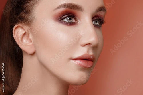 Closeup portrait of a beautiful woman on coral background. Brunette with clear skin and blue eyes. Bright makeup