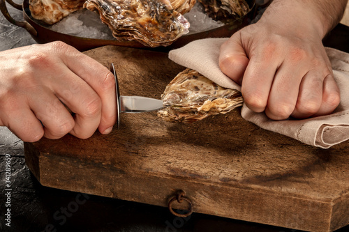 Canvas Print Shucking an oyster, man's hands holding a knife, opening oysters on a wooden boa