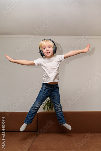 Fototapeta Naklejka Na Ścianę i Meble -  Teen boy listening to music on headphones and jumping on couch. Vertical frame