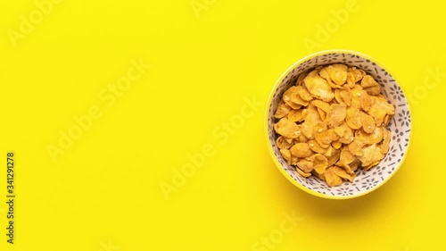 Corn Cereals in Bowl. Yellow Background with Copy Space. Stop Motion or Time Lapse in 4K. Product Presentation or Template Mockup. Overhead Top Down View.