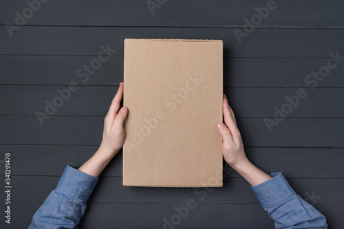 Cardboard box in children's hands on black background. Top view. Copy space