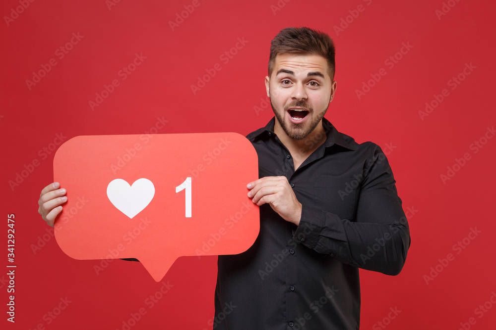 Excited young bearded guy 20s in classic black shirt posing isolated on red wall background in studio. People lifestyle concept. Mock up copy space. Hold huge like sign from social network heart form. Excited young bearded guy 20s in classic black shirt posing isolated on red wall background in studio. People lifestyle concept. Mock up copy space. Hold huge like sign from social network heart form.