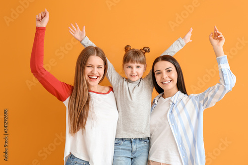 Happy lesbian couple with little adopted girl on color background