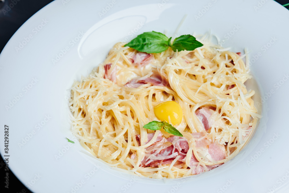 Pasta alla carbonara. Traditional italian dish spaghetti carbonara with bacon in a cream sauce in a  white plate on a dark smoky background with warm backlight. Italian cuisine. Copy space