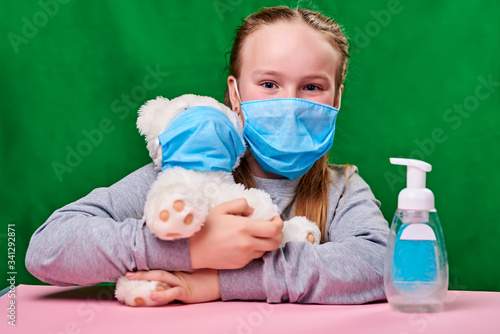 a girl wearing a blue medical mask about desenfecting the legs of a bear wearing a medical mask during quarantine. green background and pink table. covid-19. protect the health © Golovchenko Dmytro
