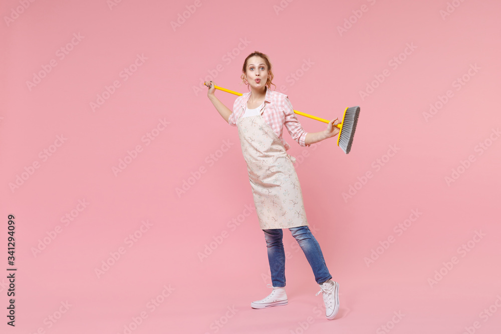 Amazed pretty young woman housewife in casual clothes, apron doing housework isolated on pastel pink wall background studio portrait. Housekeeping concept. Mock up copy space. Hold in hands broom. Amazed pretty young woman housewife in casual clothes, apron doing housework isolated on pastel pink wall background studio portrait. Housekeeping concept. Mock up copy space. Hold in hands broom.