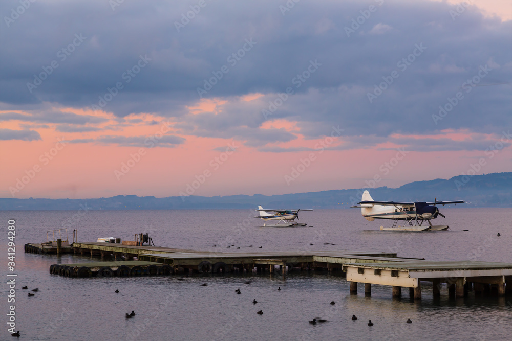 Two floatplanes on a lake at sunset, with a small pier in the foreground