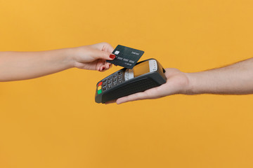 Close up cropped photo of female and male hold wireless modern bank payment terminal to process acquire credit card payments isolated on yellow background. Money, achievement, career wealth concept.