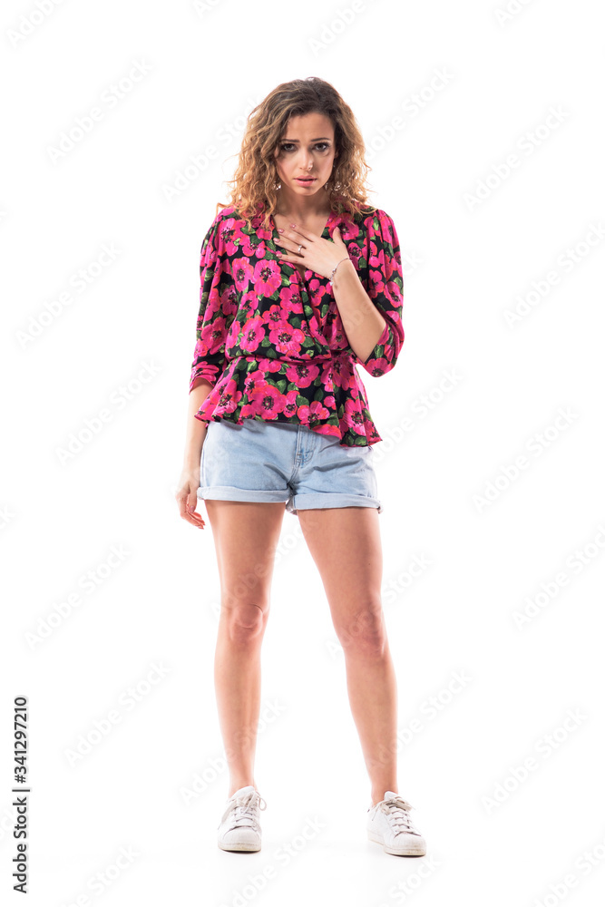 Frightened young shocked woman looking at camera with hand on heart having terrified expression. Full body isolated on white background. Frightened young shocked woman looking at camera with hand on heart having terrified expression. Full body isolated on white background.