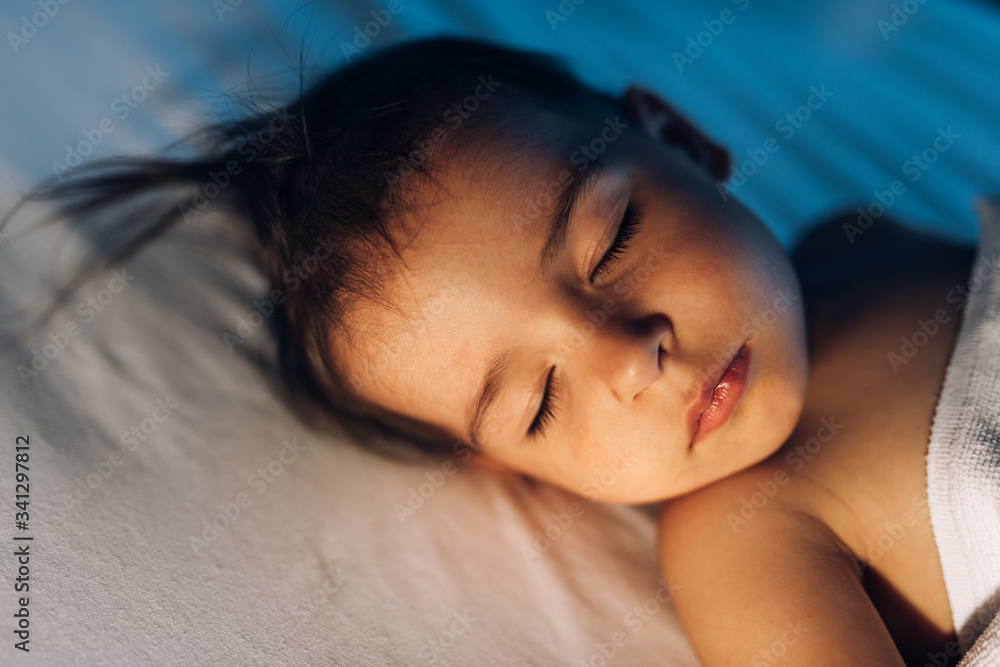 Closeup portrait of cute baby girl sleeping in white bed at night. Adorable toddler kid taking a nap in the room in lamplight. Caucasian pretty child little girl sleeps in the comfortable bed. Closeup portrait of cute baby girl sleeping in white bed at night. Adorable toddler kid taking a nap in the room in lamplight. Caucasian pretty child little girl sleeps in the comfortable bed.