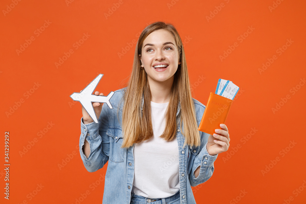 Cheerful young woman girl in casual denim clothes posing isolated on orange background studio portrait. People lifestyle concept. Mock up copy space. Hold passport ticket boarding pass paper airplane. Cheerful young woman girl in casual denim clothes posing isolated on orange background studio portrait. People lifestyle concept. Mock up copy space. Hold passport ticket boarding pass paper airplane.