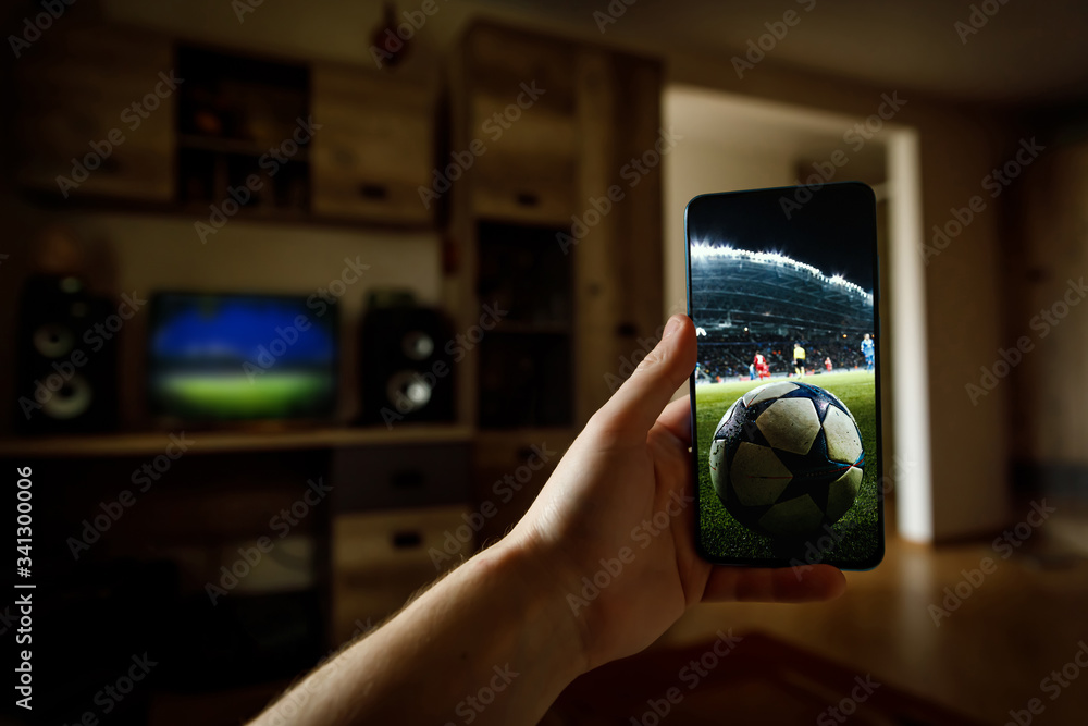 Watching football game at home via smartphone. Broadcasting soccer from the stadium. Stock Photo Adobe Stock