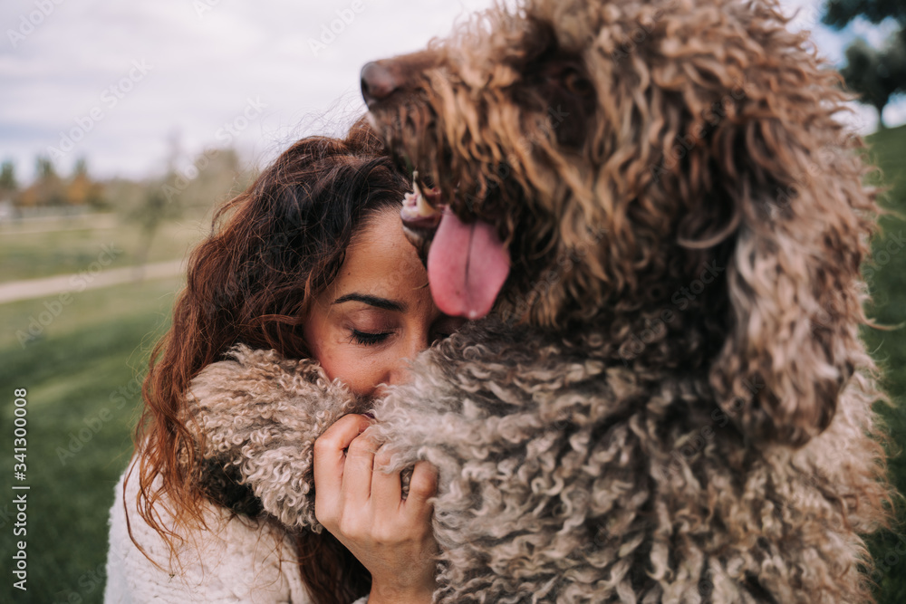 A beautiful woman is in the meadow with her dog. They are hugging. She has her eyes closed while the doggy is looking far. They are enjoying their company. The pet is a Spanish water dog. A beautiful woman is in the meadow with her dog. They are hugging. She has her eyes closed while the doggy is looking far. They are enjoying their company. The pet is a Spanish water dog.