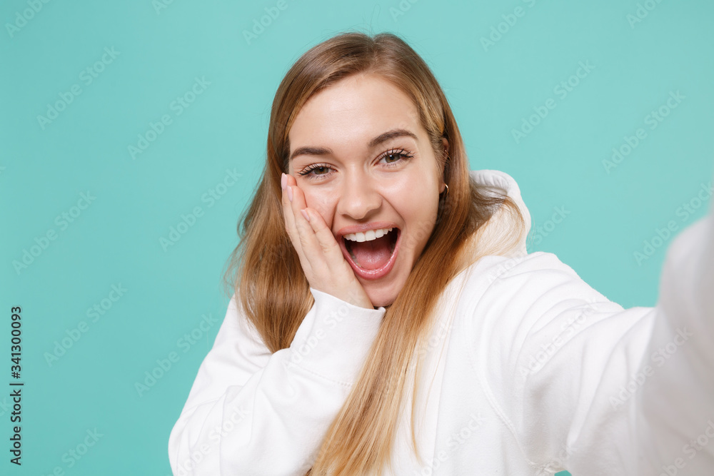 Close up of excited young woman girl in casual white hoodie isolated on blue turquoise background. People lifestyle concept. Mock up copy space. Doing selfie shot on mobile phone, put hand on cheek. Close up of excited young woman girl in casual white hoodie isolated on blue turquoise background. People lifestyle concept. Mock up copy space. Doing selfie shot on mobile phone, put hand on cheek.